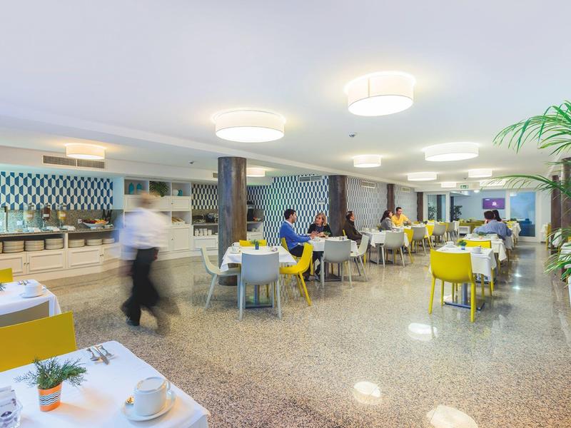 Sala da pranzo dell'hotel luminosa con sedie gialle e grigie e pavimento lucido.