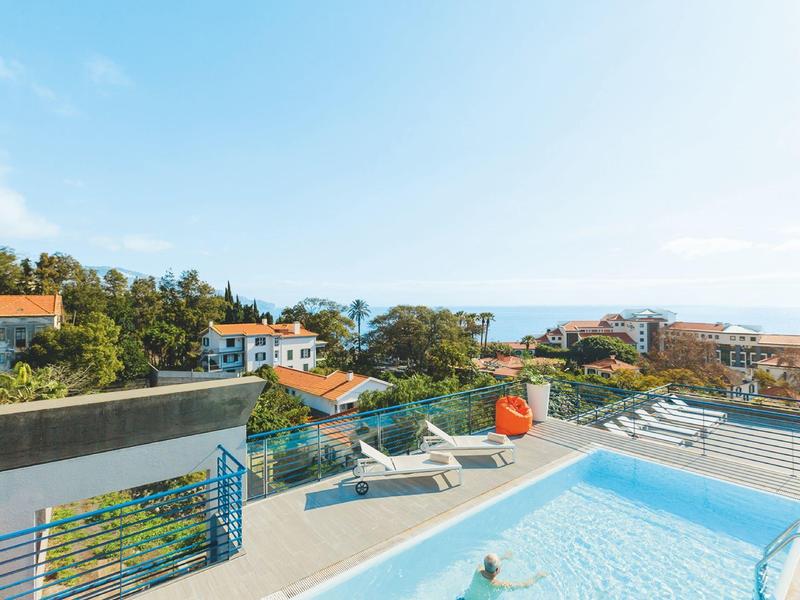 Piscina sul tetto con lettini, vista su case e mare sotto un cielo limpido.