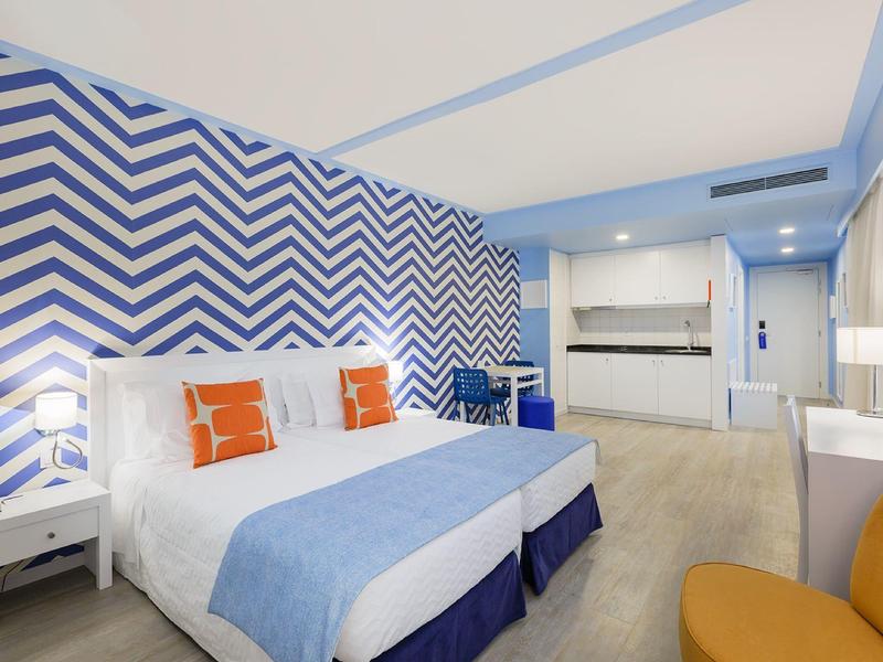 Camera d'hotel con parete a chevron blu e bianca, letto grande, angolo cottura e arredamento moderno.