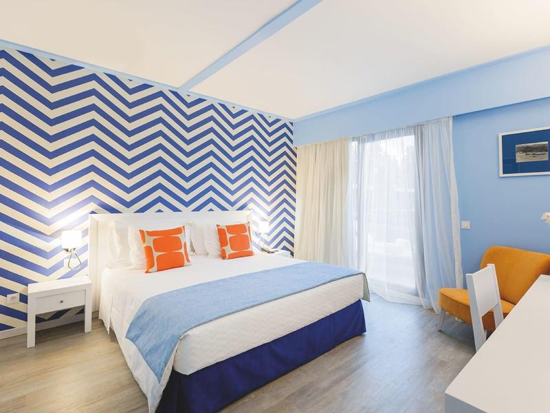 Camera d'hotel luminosa con letto king, parete a motivi e poltrone arancioni.