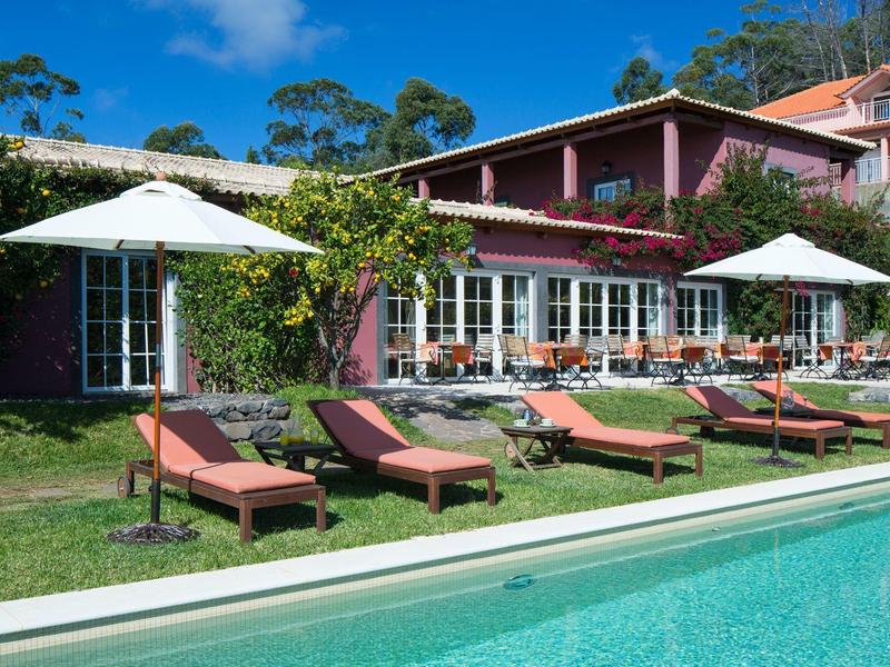 Klidná oblast u bazénu s lehátky a slunečníky před budovou hotelu.