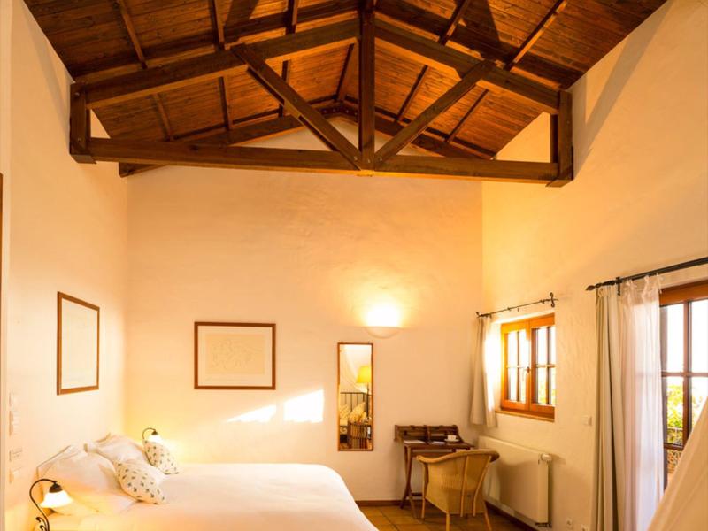 Příjemný hotelový pokoj s dřevěným trámovým stropem, velkou postelí a okny pro denní světlo.