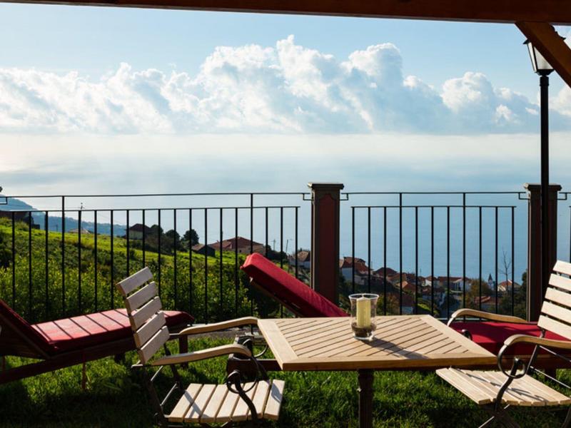 Balkon s dřevěným nábytkem s výhledem na moře a hory za jasné oblohy.