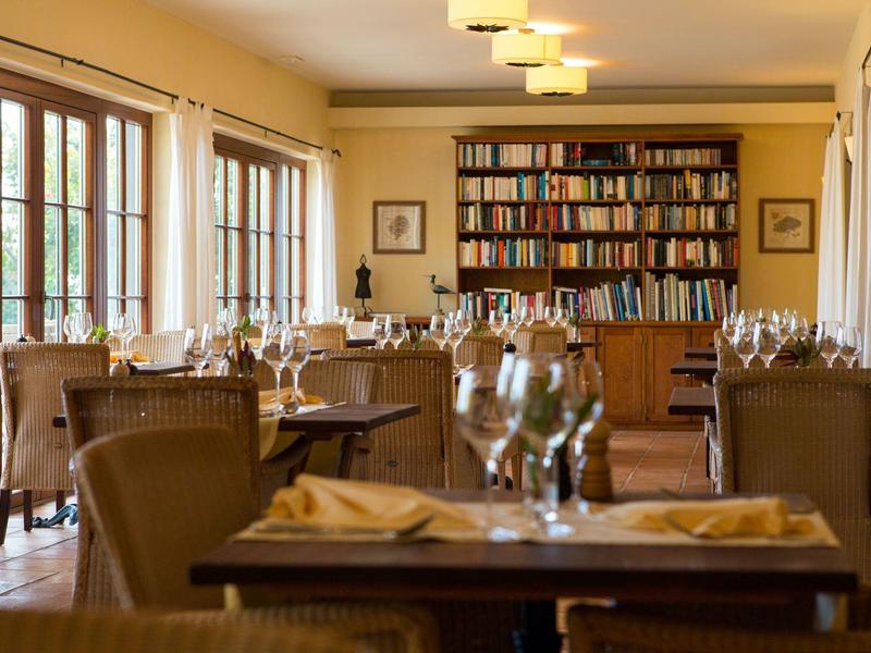 Příjemná jídelna s dřevěným nábytkem a knihovnou, světlá díky oknům.