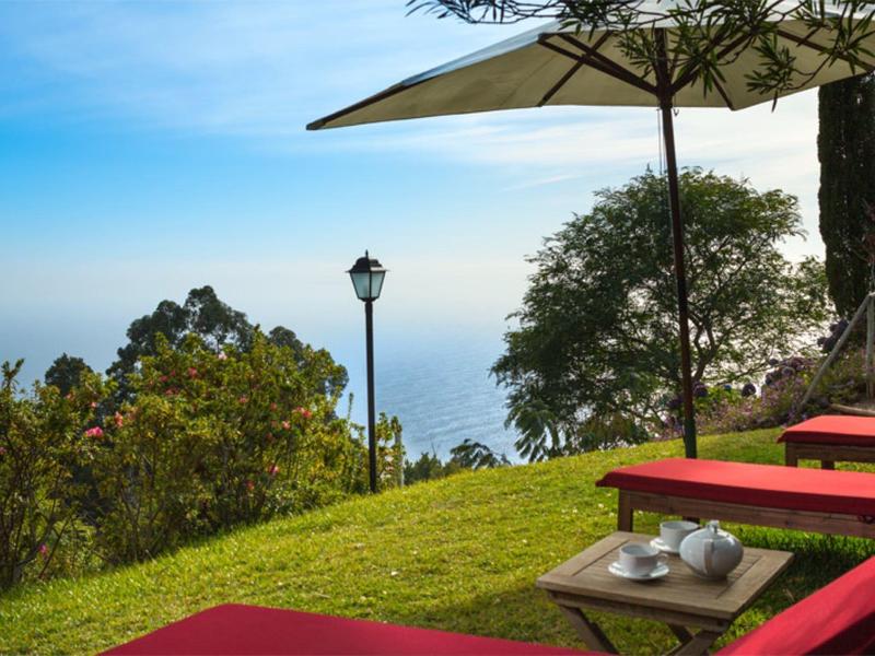 Klidná zahrada s červenými lehátky s výhledem na moře za jasné oblohy.