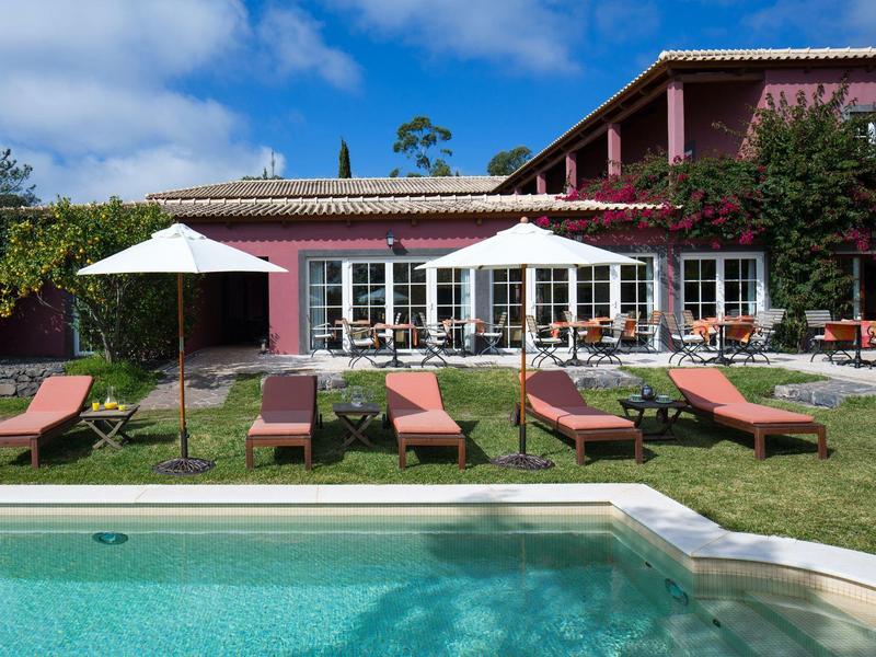 Bazén s lehátky a slunečníky před dvoupodlažním červeným rekreačním domem.