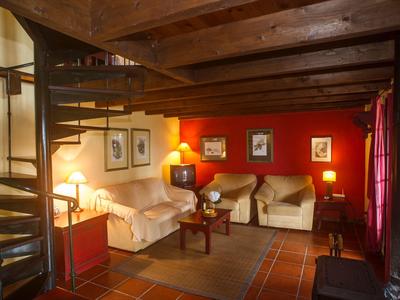 Cozy living room with sofas, glowing lamps, red wall, and wooden spiral staircase.