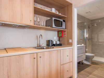 Compact hotel kitchenette with microwave, coffee maker, and adjacent bathroom with shower.