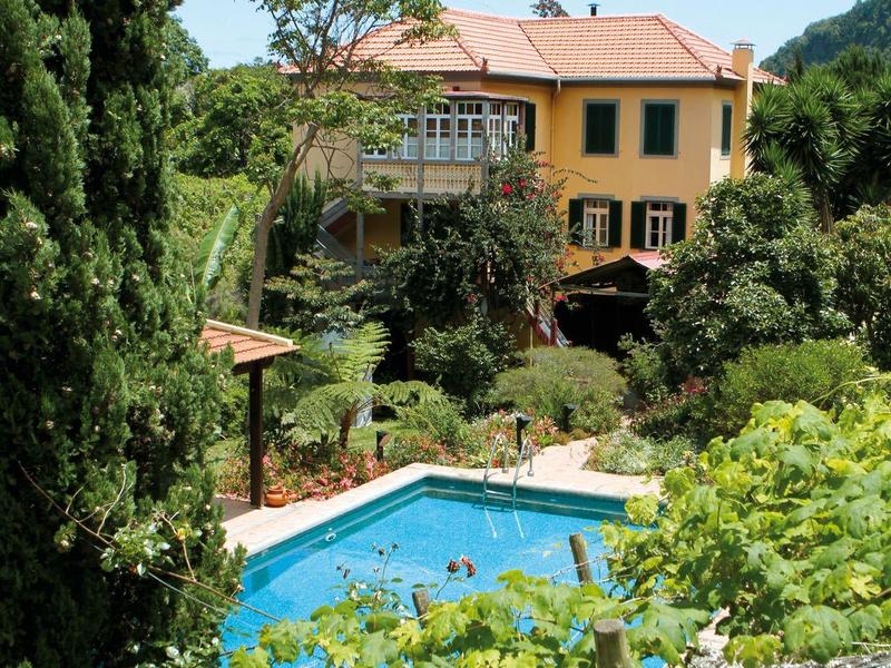 Hotel with yellow building and outdoor pool surrounded by green trees and plants.