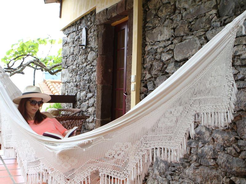 Woman relaxing in a white hammock in front of a stone house wall.