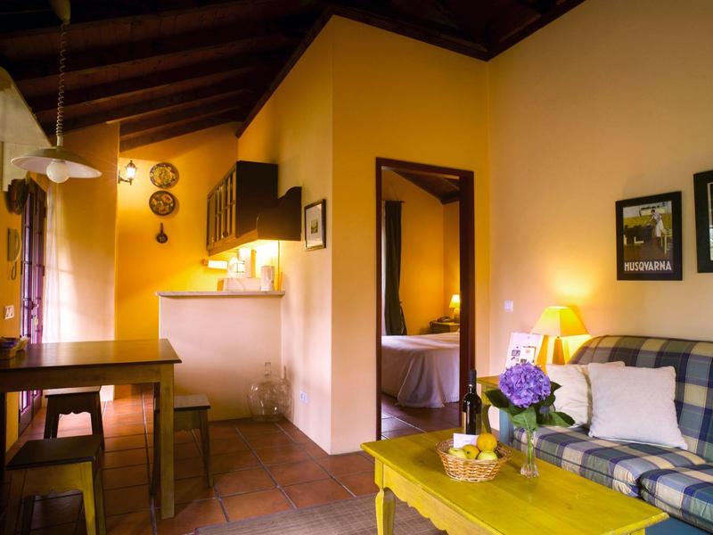 Cozy living room with sofa, yellow table, and adjacent open kitchen in warm lighting.