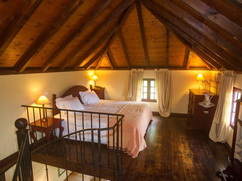 Cozy attic room with wooden beams, double bed, nightstands, and soft lamp lighting.