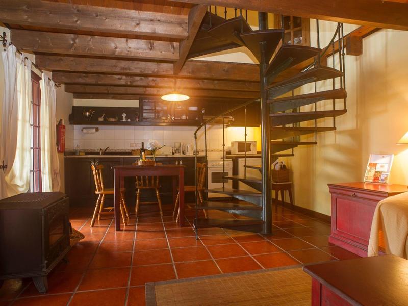 Cozy living area with spiral staircase, wooden beams, and kitchenette illuminated by warm light.