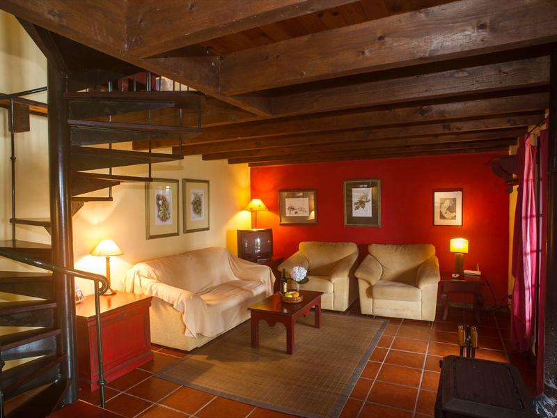 Cozy living room with sofas, glowing lamps, red wall, and wooden spiral staircase.