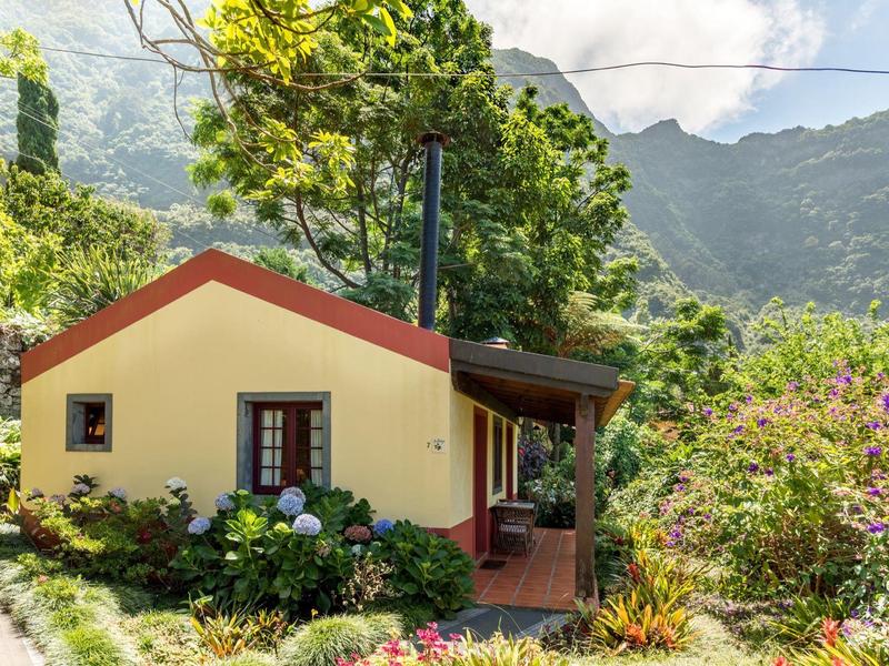 Small yellow house with garden and mountains in the background, ideal for vacation.