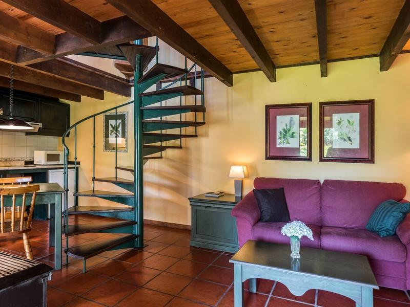Cozy living area with purple sofa, spiral staircase, and wooden beam ceiling.