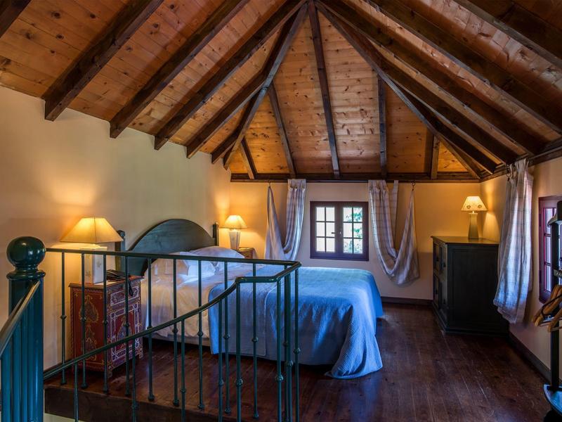 Cozy bedroom under wooden slanted roof with double bed and warm lighting.