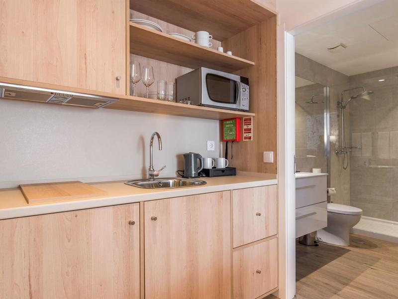 Compact hotel kitchenette with microwave, coffee maker, and adjacent bathroom with shower.