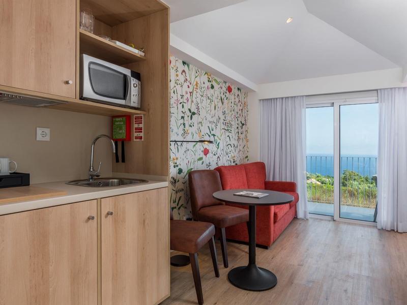 Small hotel room seating area with red sofa, round table, and kitchenette with microwave