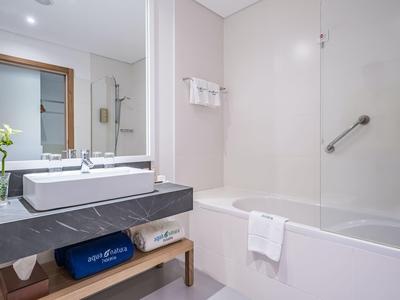 Helles Badezimmer mit grauer Holzarbeitsplatte, rechteckigem Waschbecken, Badewanne und großem Spiegel.