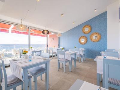 Helles Restaurant mit blau-weißer Einrichtung, Tischen mit weißen Tüchern und großer Fensterfront.