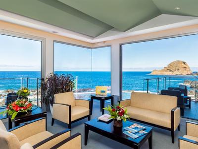 Moderner Lounge-Bereich mit hellen Möbeln und Panoramafenstern mit Blick auf das blaue Meer und Felsen.