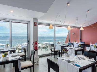 Modernes Restaurant mit weißen Tischtüchern und Meerblick durch große Fensterfront.