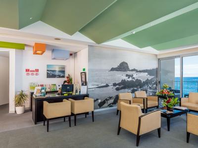 Helles Wartezimmer mit beigen Sesseln, Meerblick und Wandbild einer Küstenlandschaft.