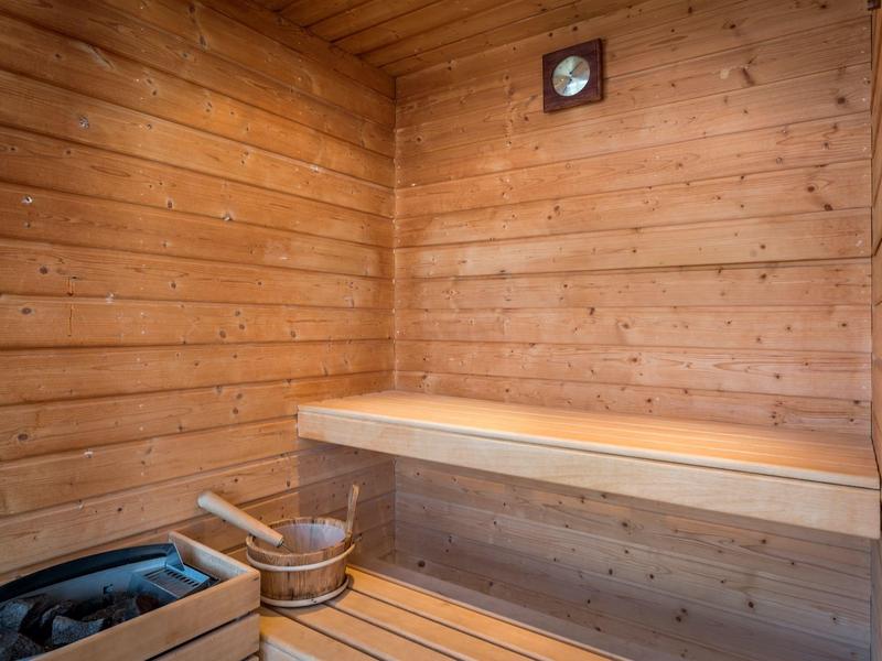 Kleine Holzsauna mit Holzbänken, Eimer, Aufgusslöffel und einer Uhr an der Wand.