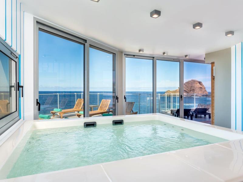 Moderner Innenwhirlpool mit Panoramafenstern, Blick auf Meer und Felsen, helle, klare Raumgestaltung.