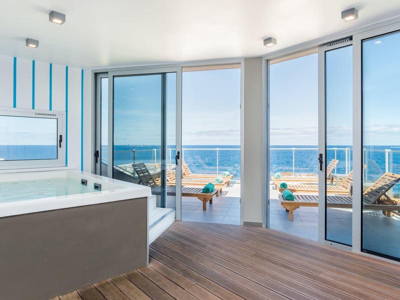 Moderner Raum mit Whirlpool, Holzfußboden und großen Glasfenstern mit Blick auf Terrasse und Meer.