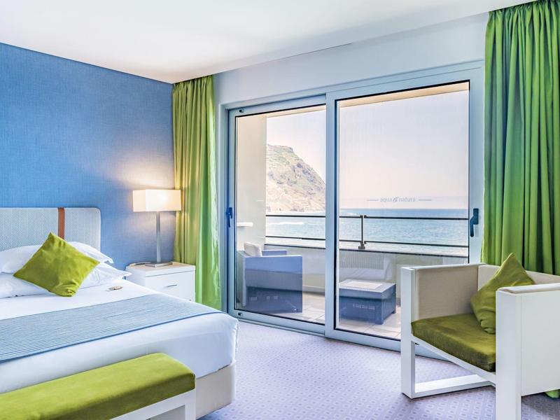 Hell eingerichtetes Schlafzimmer mit grün-weißem Farbschema und Blick auf das Meer.