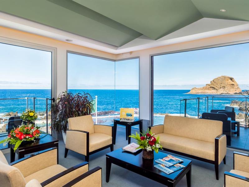 Moderner Lounge-Bereich mit hellen Möbeln und Panoramafenstern mit Blick auf das blaue Meer und Felsen.