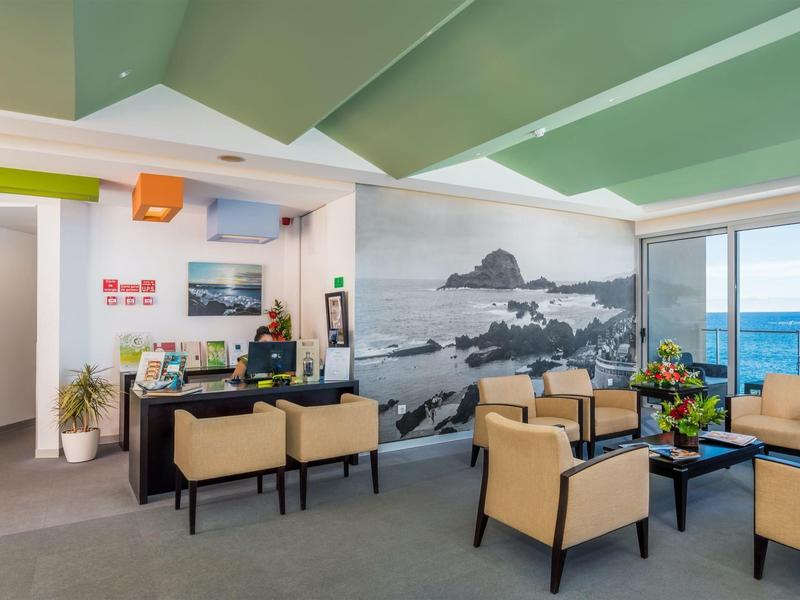 Helles Wartezimmer mit beigen Sesseln, Meerblick und Wandbild einer Küstenlandschaft.