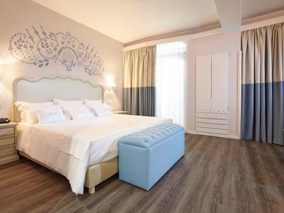 Camera d'hotel luminosa con grande letto, panca blu e pavimento in legno moderno.