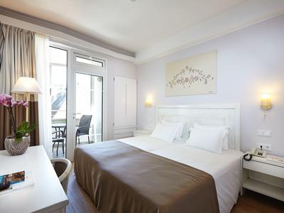 Helles, modernes Schlafzimmer mit großem Doppelbett, Balkontür, weißen Möbeln und brauner Bettdecke.