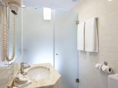 Bagno moderno con lavabo, asciugacapelli e porta in vetro per la doccia, design luminoso e bianco.