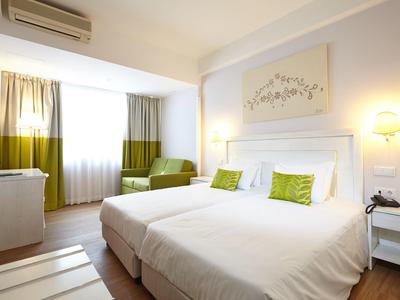 Camera d'hotel luminosa con letto matrimoniale, decorazione verde-bianca e ampia finestra.