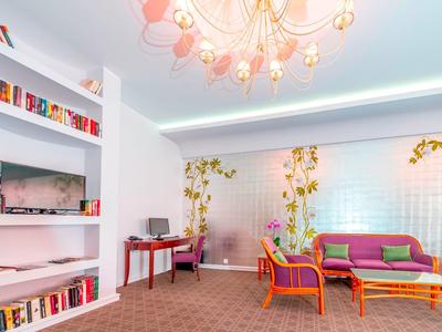 Area lounge luminosa con poltrone colorate, divano, scaffali per libri e decorazioni floreali sul muro.