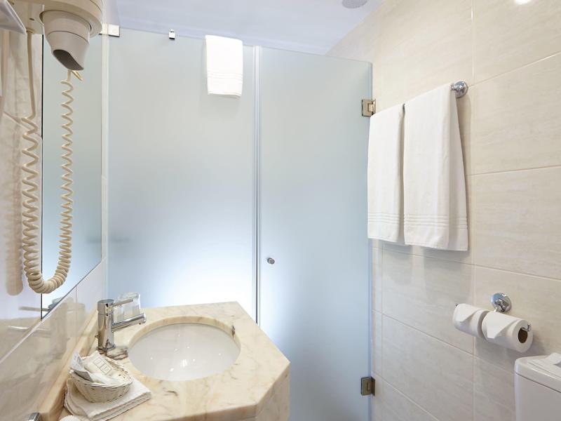 Bagno moderno con lavabo, asciugacapelli e porta in vetro per la doccia, design luminoso e bianco.