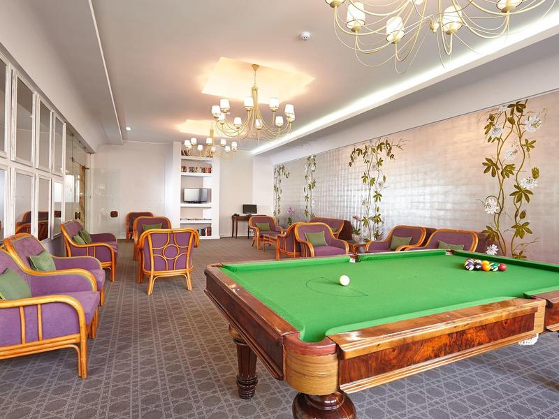 Sala giochi elegante con tavolo da biliardo verde, poltrone colorate e decorazione murale artistica.