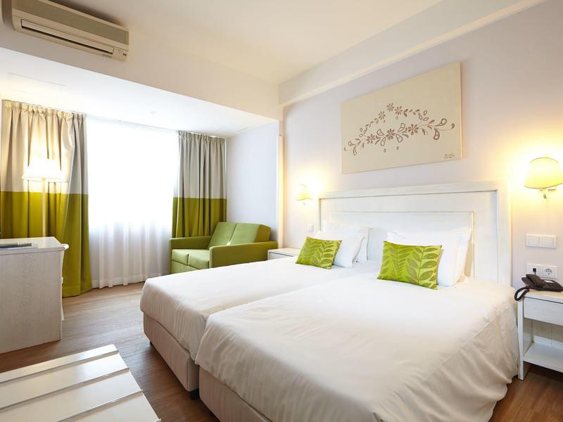 Camera d'hotel luminosa con letto matrimoniale, decorazione verde-bianca e ampia finestra.