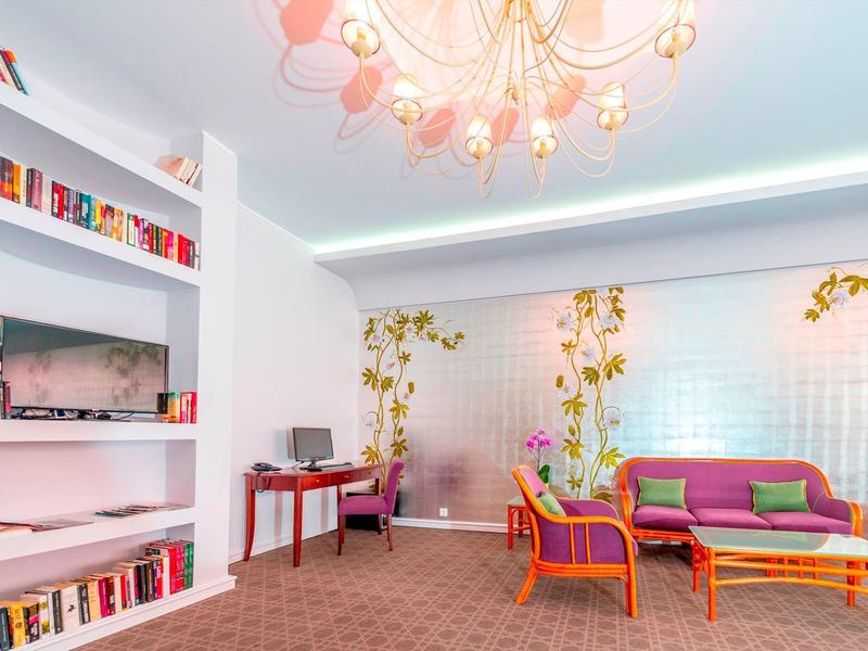 Area lounge luminosa con poltrone colorate, divano, scaffali per libri e decorazioni floreali sul muro.