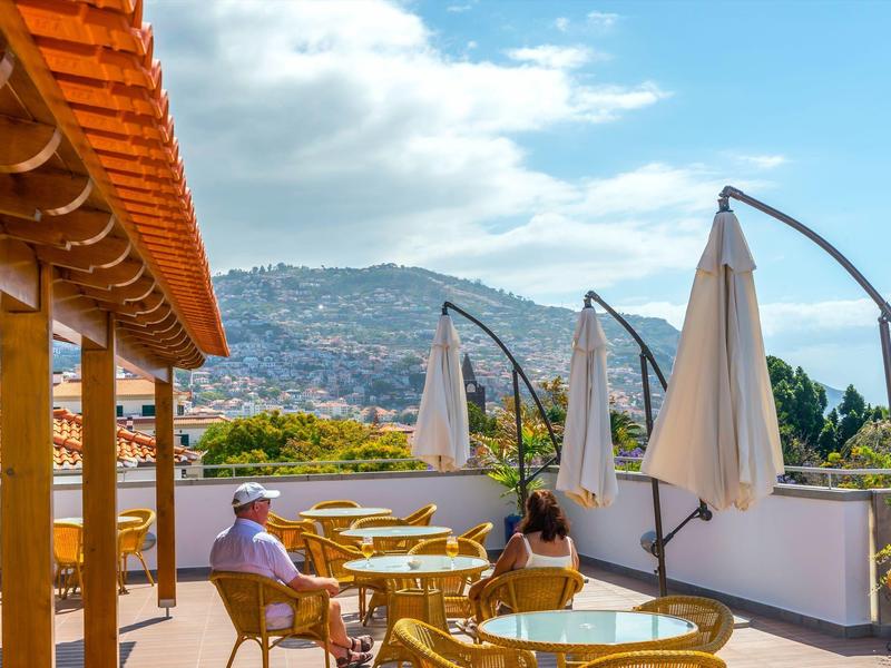 Terrazza sul tetto con tavoli, sedie e ombrelloni, paesaggio montano sullo sfondo.