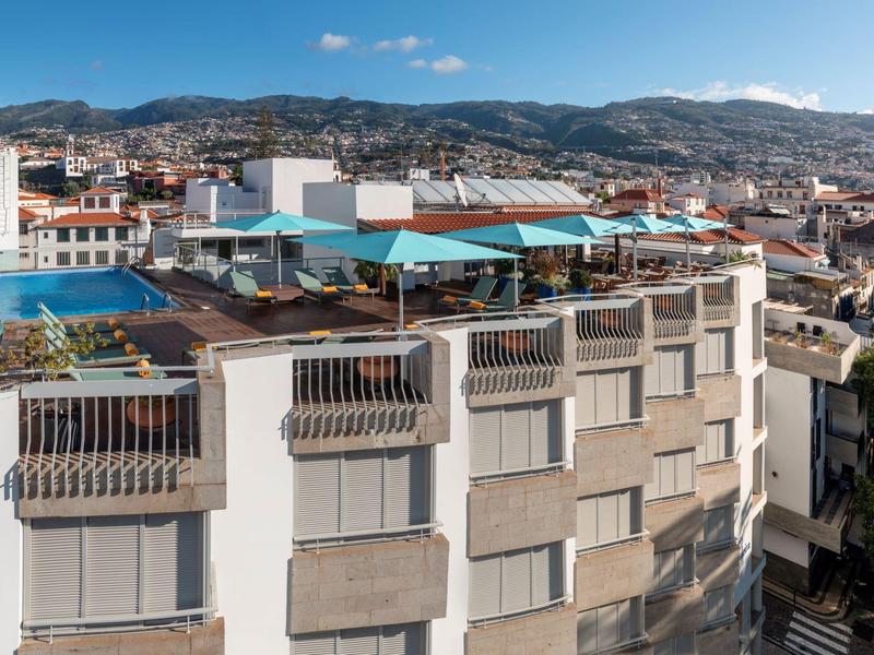 Terrazza sul tetto con piscina e ombrelloni su un edificio con vista sulla città e le montagne.
