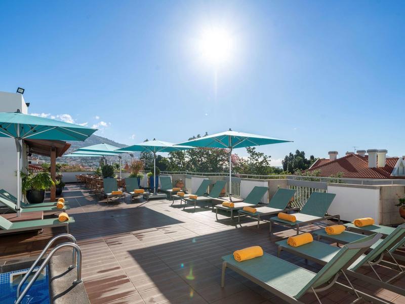 Terrazza panoramica con lettini e ombrelloni sotto un cielo azzurro.