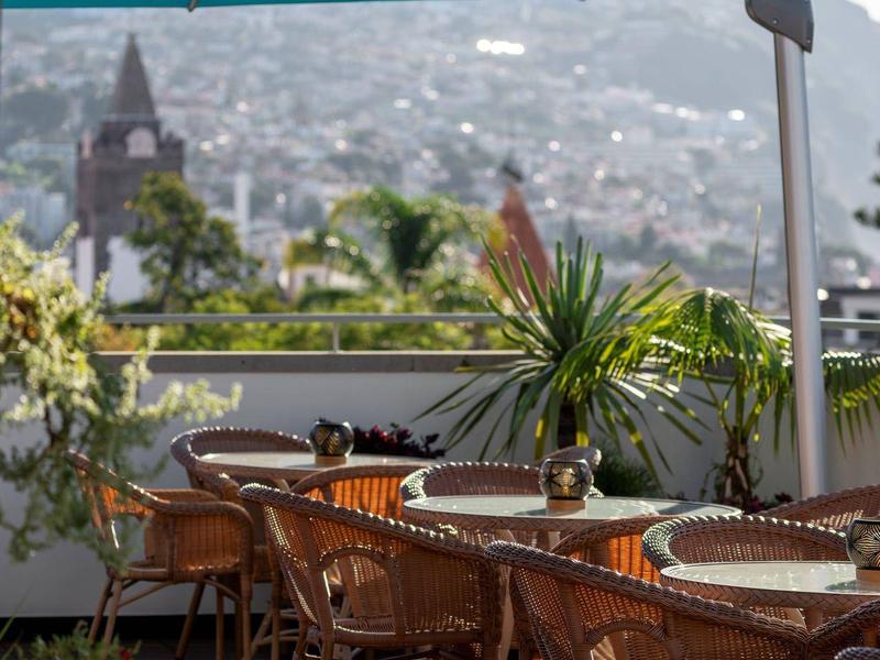 Terrazza con sedie e tavoli sotto ombrelloni blu con vista sulla città.