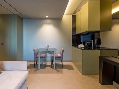 Moderner Wohnbereich mit grünem Küchenblock, Glastisch, Stühlen und beigem Sofa.