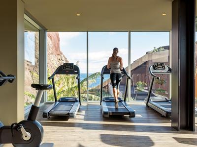 Modern gym with treadmills and panoramic window overlooking rocks and nature.