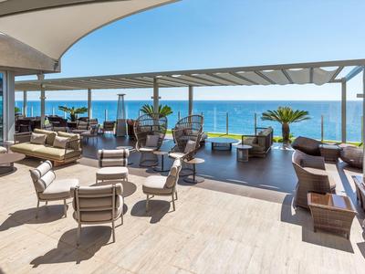 Offener Terrassenbereich mit modernen Sitzmöbeln, Palmen und Meerblick bei klarem Himmel.